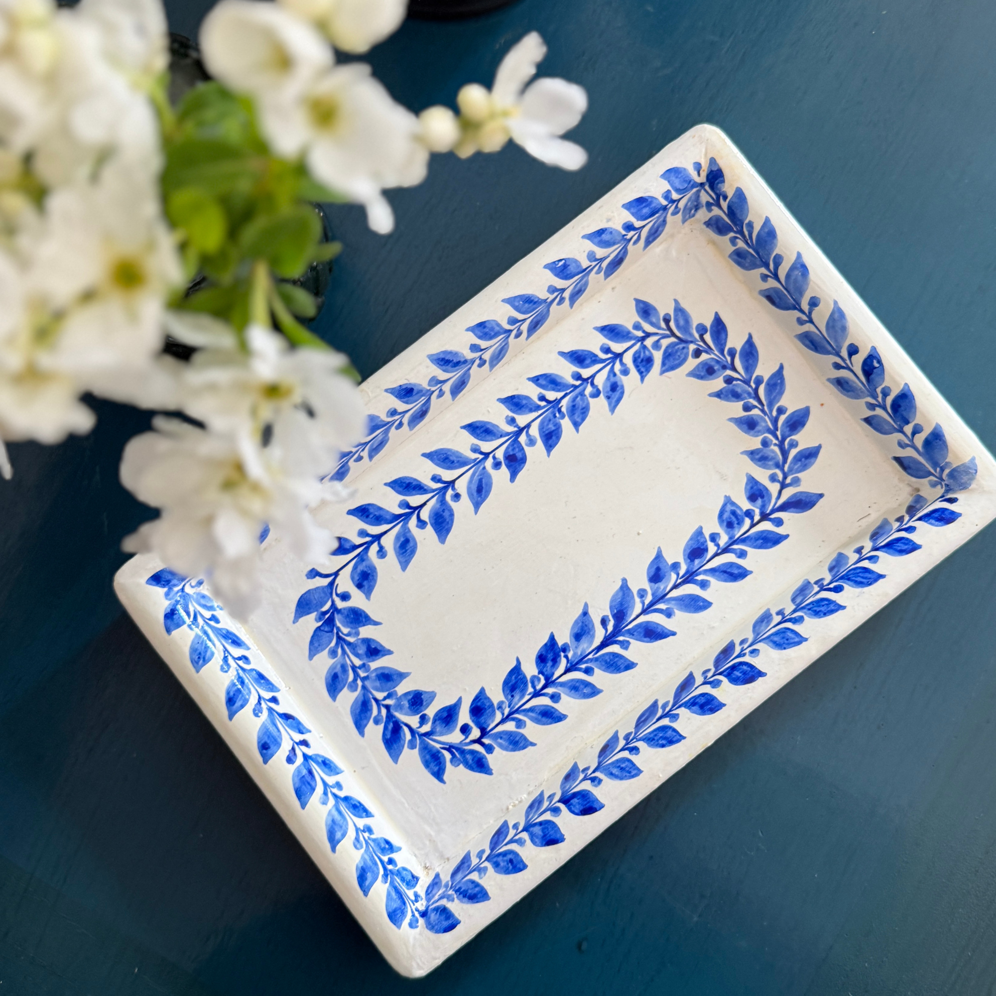 Decorative tray with blue leaf patterns on a dark surface with white flowers.