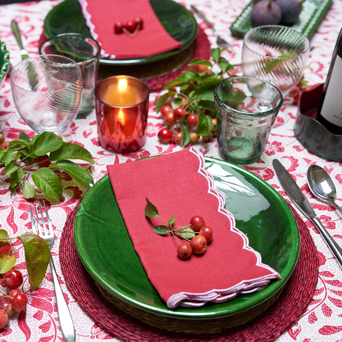 Dining table set with green plates, red napkins, and festive decorations on a patterned tablecloth.
