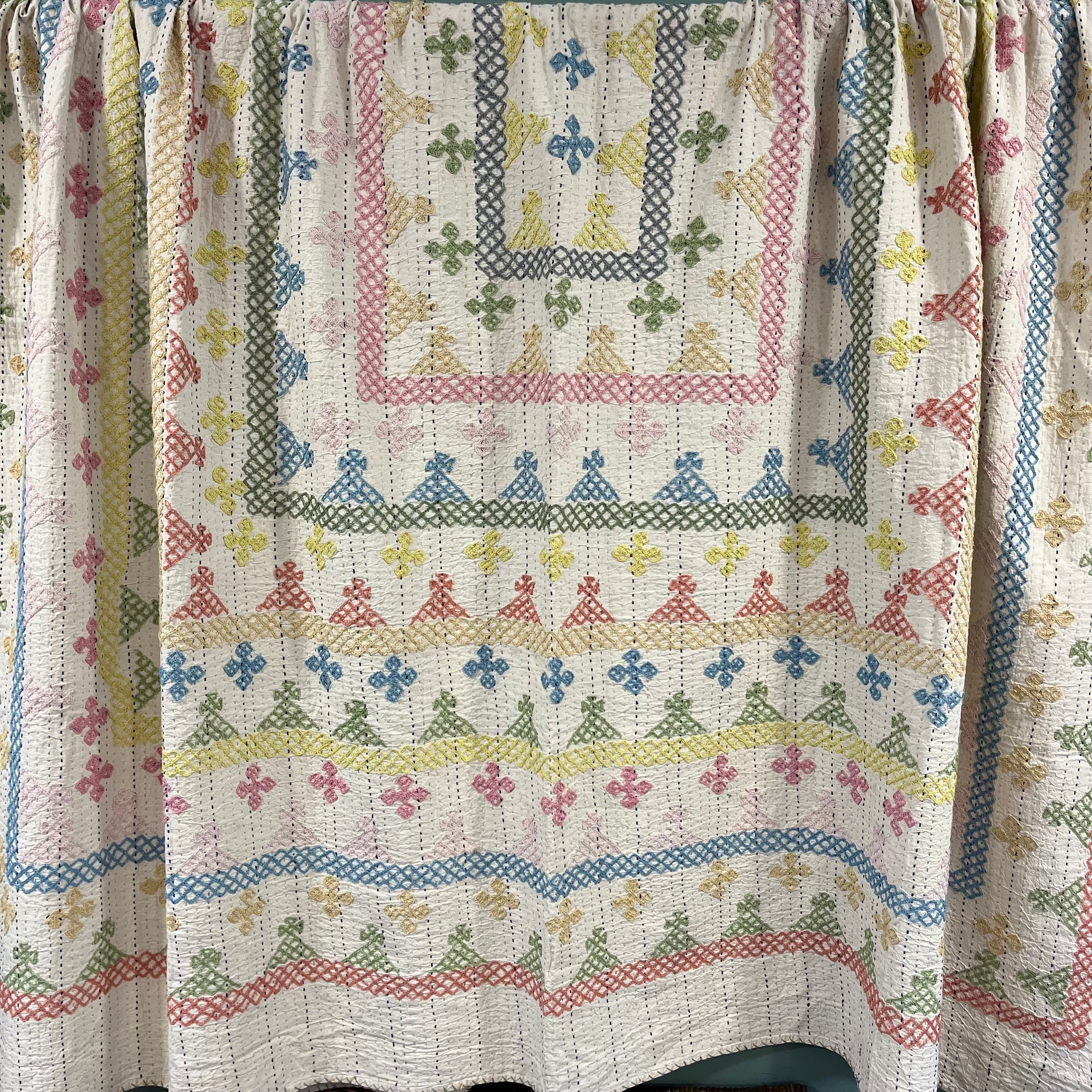 Decorative quilt with cross-stitch patterns in various colors on a white background